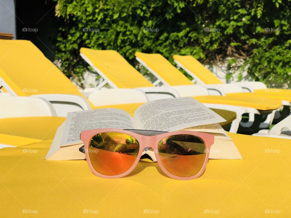 Pink sunglasses and a book placed on a yellow sunbed with many yellow sunbeds in the background