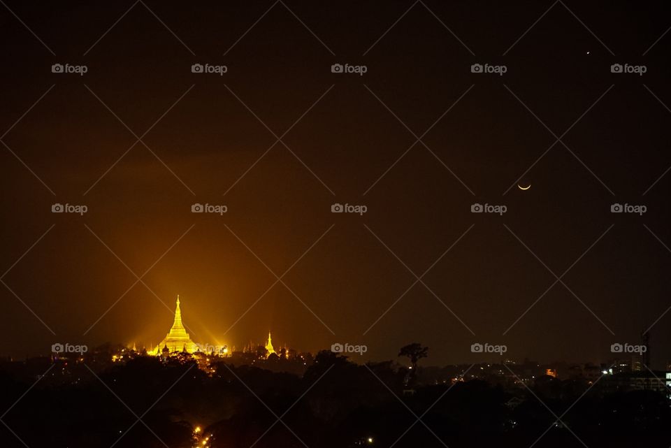 Yangon, Myanmar at night. Lights make the Shwedagon Pagoda shine next to the crescent moon.