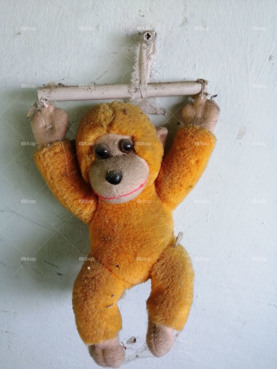 Old dirty soft toy orange monkey with his hands up on a stick