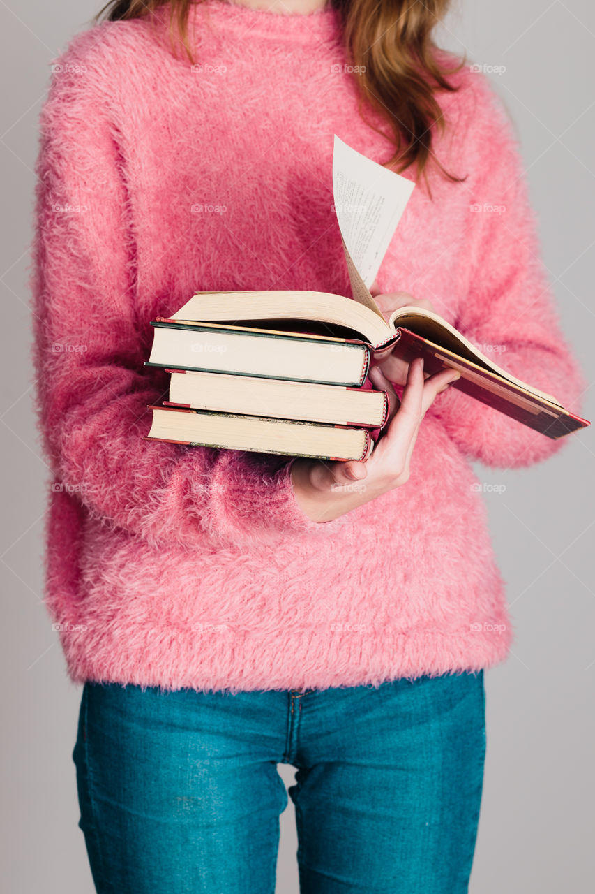 Young girl holding a few books. Teenager girl wearing pink sweater and blue jeans. Vertical photo