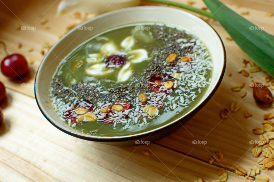 Close-up detail of beautiful sweet green smoothie bowl decorated with cherry, oatmeal, almond, coconut and chia with yogurt white flower design gourmet smoothie food photography background 
