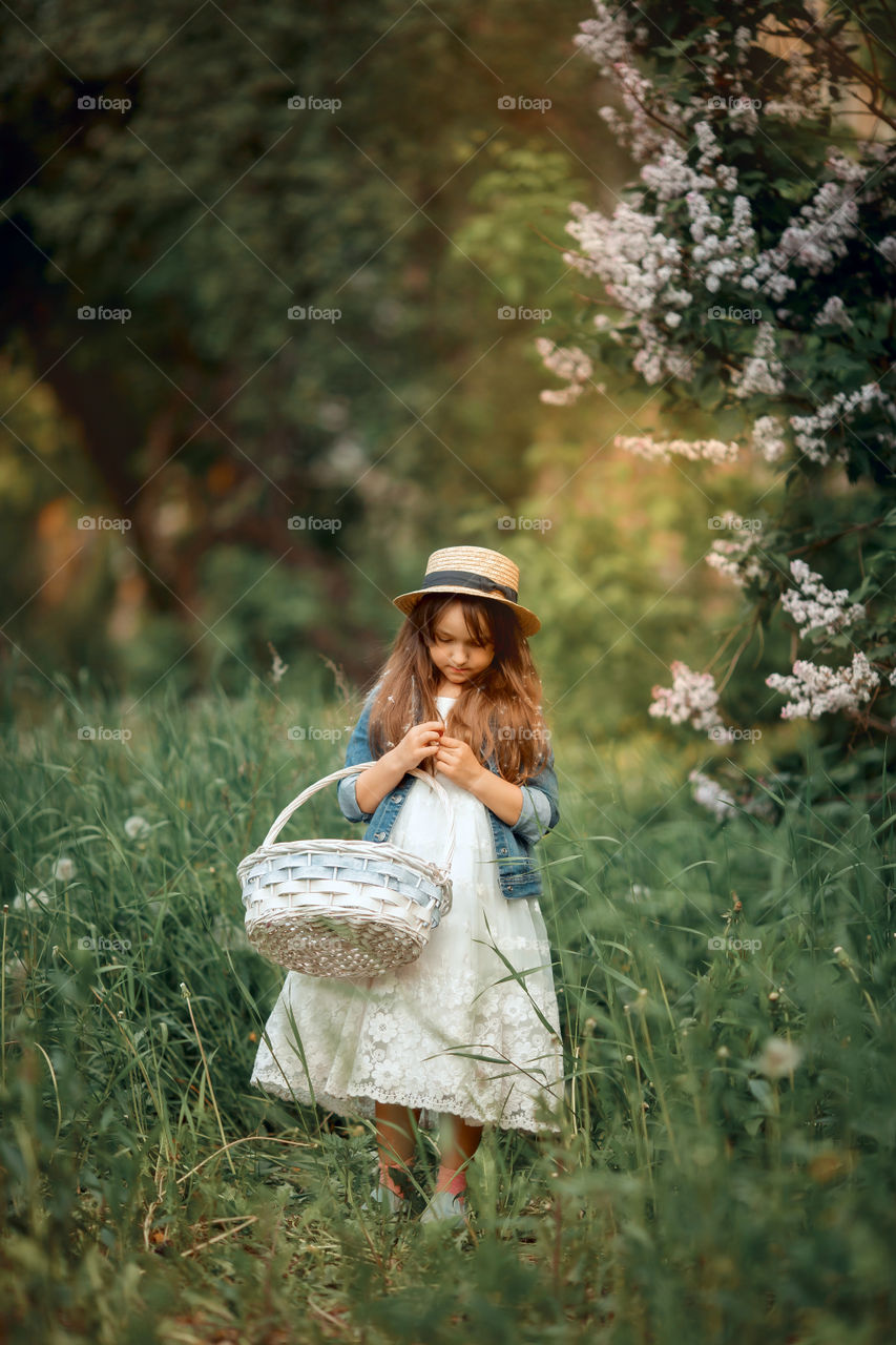 Little girl in a hat near blossom lilac tree at sunset 