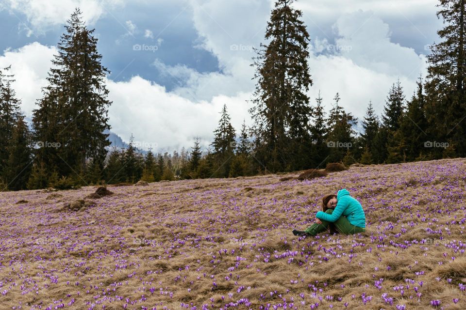 Woman while on a hike in the mountains, laying in a meadow full with crocus flowers.