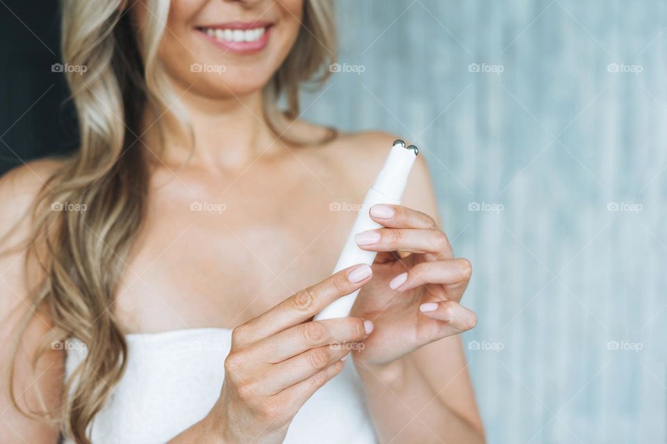 Beauty portrait of happy blonde smiling woman with clean fresh face and hands with long hair doing fasial massage with microcurrent facial massager at the bath room, home body care