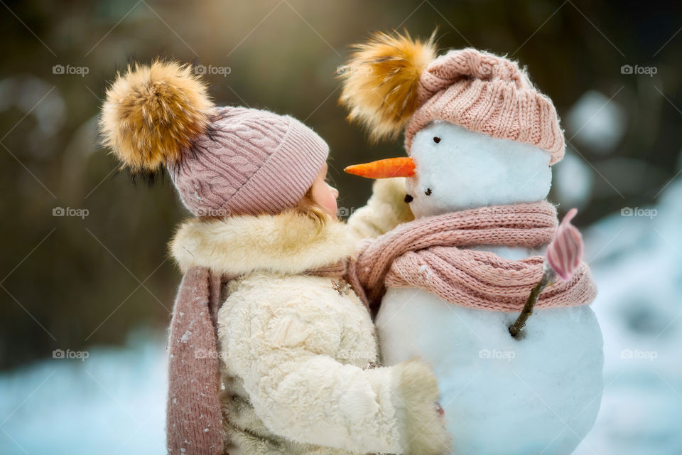 Little girl with snowman in winter forest at sunny day