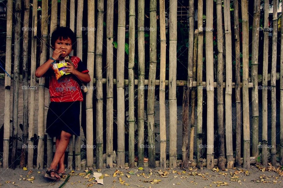 Kid standing by a fence eating