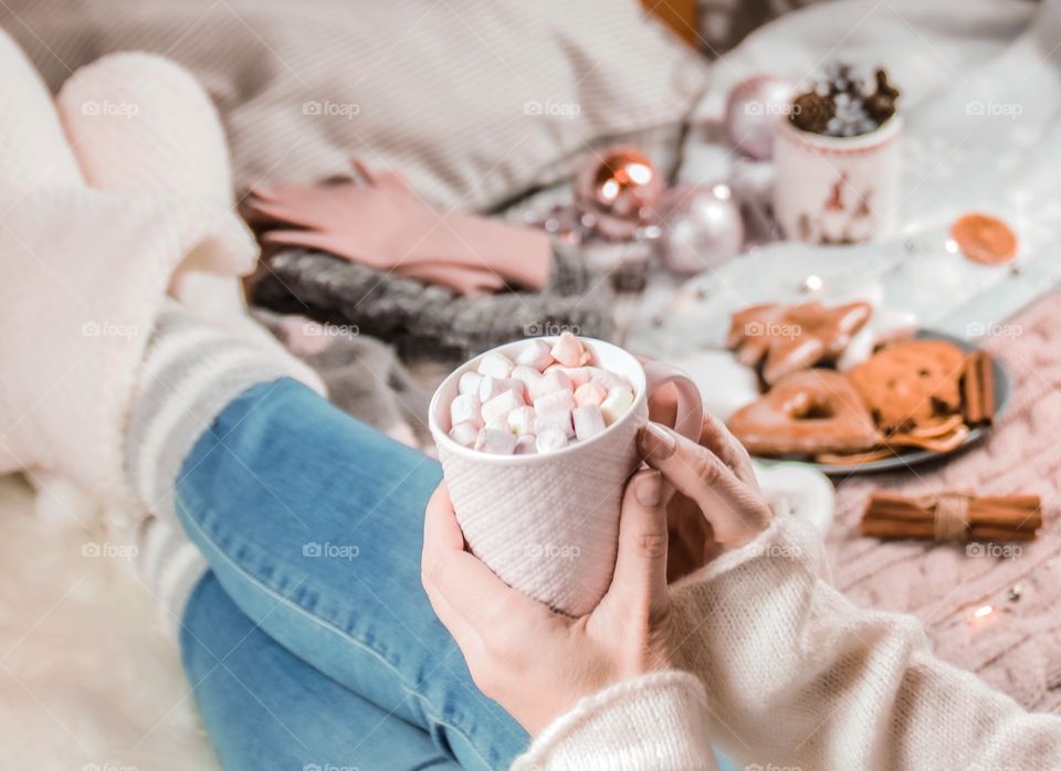 Cup with marshmallows in female hands on a background of Christmas decor