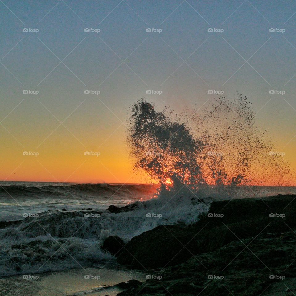 Wave crashing on rock during sunset