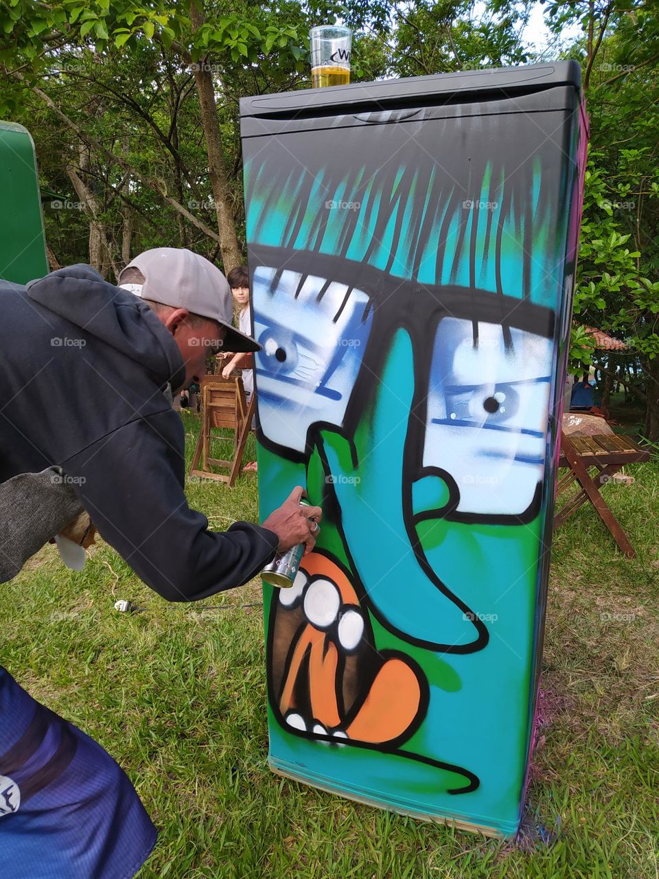 Artista grafitando geladeira em camping.