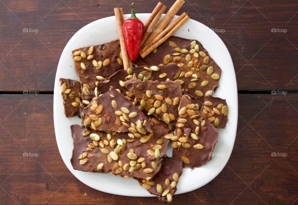 More Chocolate - Cinnamon Chocolate Chili Bark with cinnamon sticks and red chili pepper on a white plate, dark wood background 