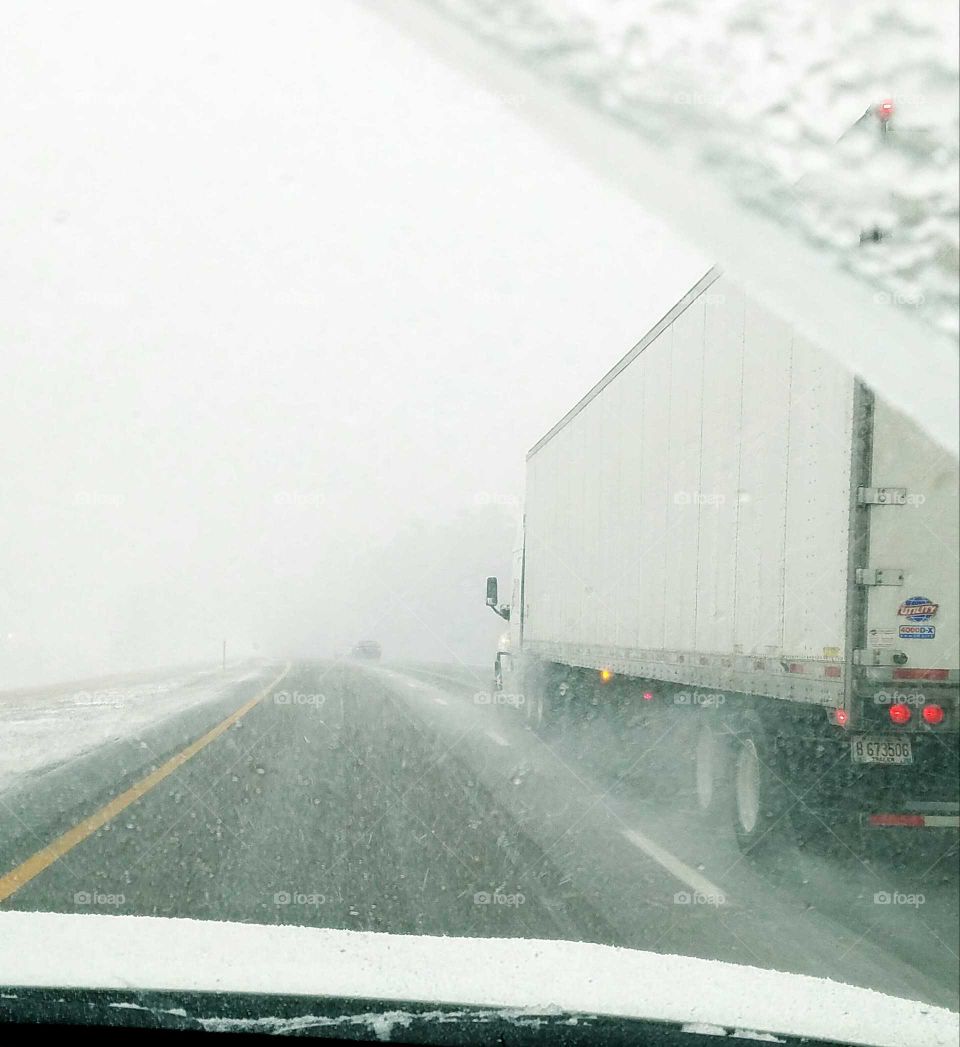 Passing big rig in snowstorm on highway.