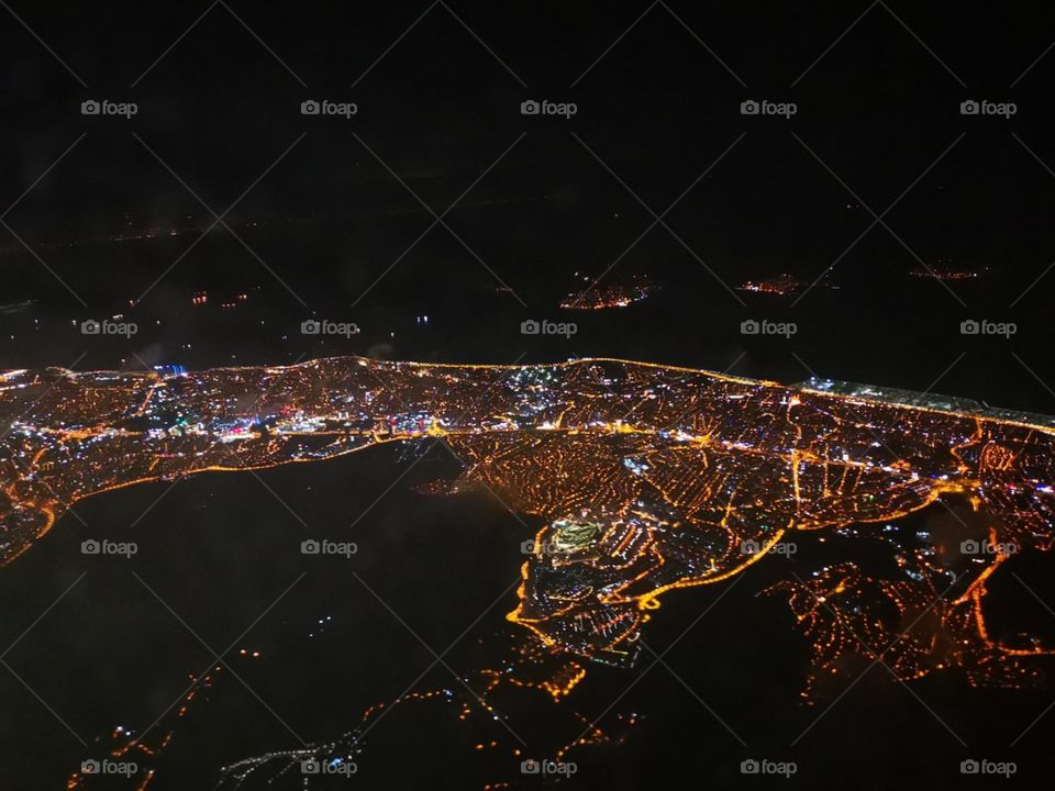 Artificially iluminated big city night view with black coloured sea night view. From the airplane.