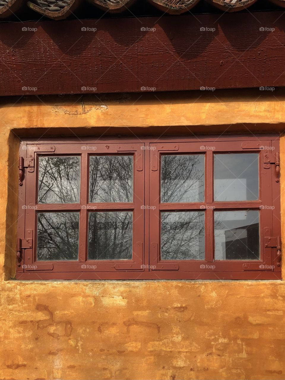 Old house with orange brick wall and red window. Reflection in the glass.