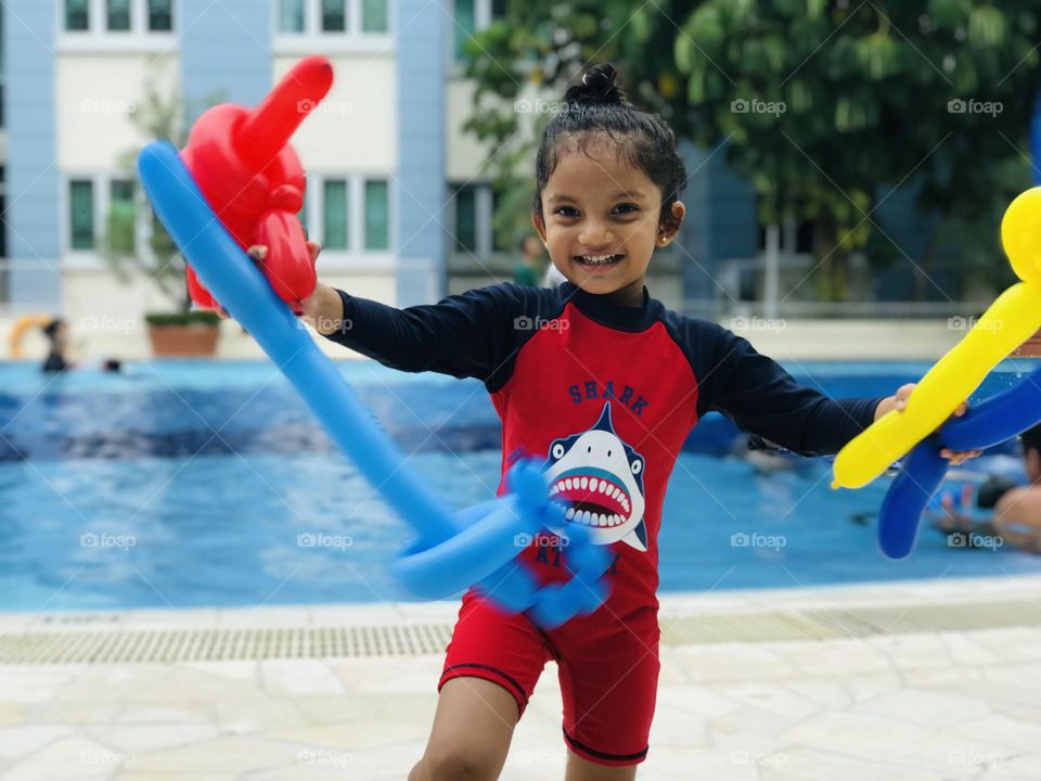 Girl enjoying at swimming pool with balloons and she smiles.