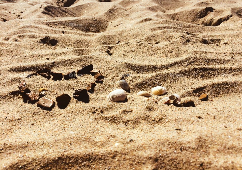 Love heart made with stones and shells on a sand