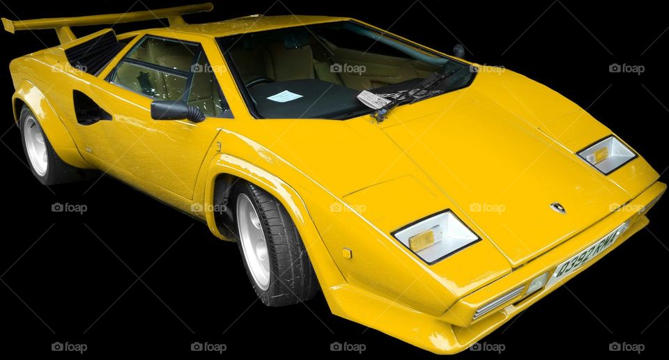 ISOLATED on BLACK,  
 Yellow Lamborghini Countach

 is a mid-engined, V12 sports car produced by Italian car manufacturer Lamborghini from 1974 to 1990. Its design pioneered and popularized the wedge-shaped, sharply angled look popular in many high-performance sports cars. It also popularized the "cab forward" design concept, which pushes the passenger compartment forward to accommodate a larger engine.

In 2004, American car magazine Sports Car International named the car number three on the list of Top Sports Cars of the 1970s, and listed it number ten on their list of Top Sports Cars of the 1980s.

The rear wheels were driven by a traditional Lamborghini V12 engine mounted longitudinally with a mid-engined configuration. This contrasted with the Miura with its centrally mounted, transversely-installed engine. For better weight distribution, the engine is pointed "backwards"; the output shaft is at the front, and the gearbox is in front of the engine, the driveshaft running back through the engine's sump to a differential at the rear. Although originally planned as a 5 L (310 cu in) powerplant, the first production cars used the Lamborghini Miura's 4-liter engine. Later advances increased the displacement to 4754 cc and then (in the "Quattrovalvole" model) 5167 cc with four valves per cylinder.

All Lamborghini Countaches were equipped with six Weber carburetors until the arrival of the 5000QV model, at which time the car became available in America, and used Bosch K-Jetronic fuel injection. The European models, however, continued to use the carburetors (producing more power than fuel-injected cars) until the arrival of the Lamborghini Diablo, which replaced the Countach.