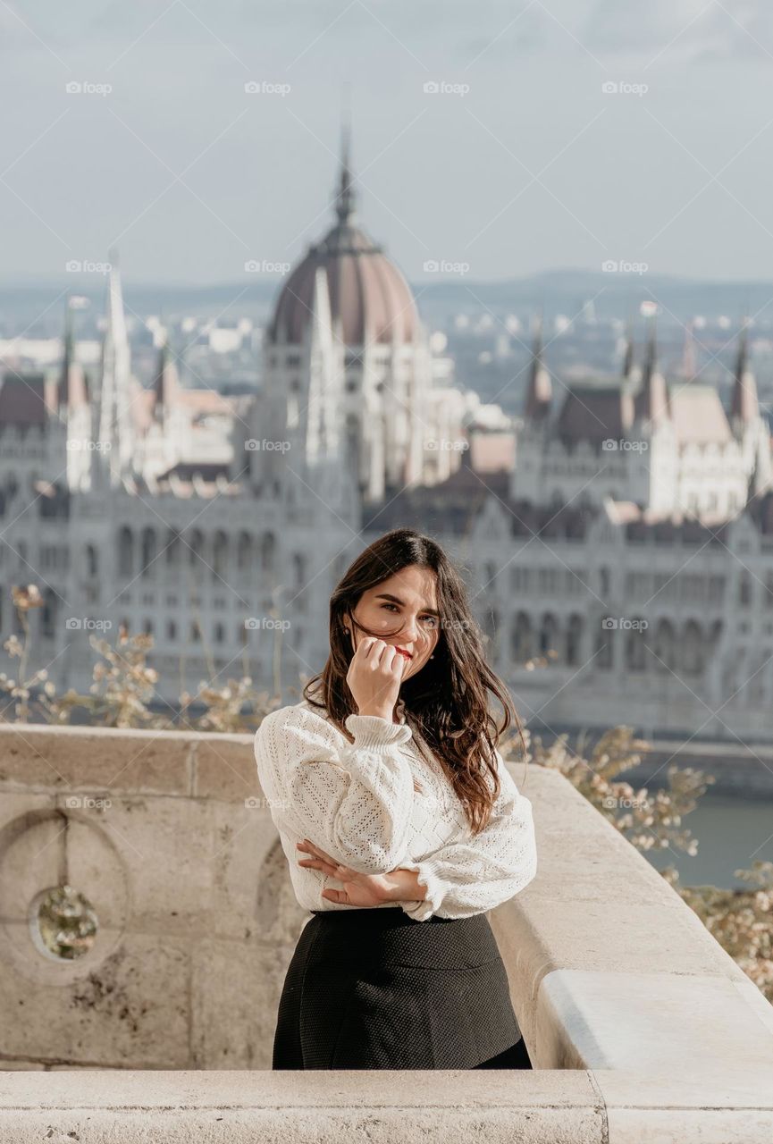 Portrait of pretty girl standing on balcony overlooking city of Budapest and the Hungarian parliament building