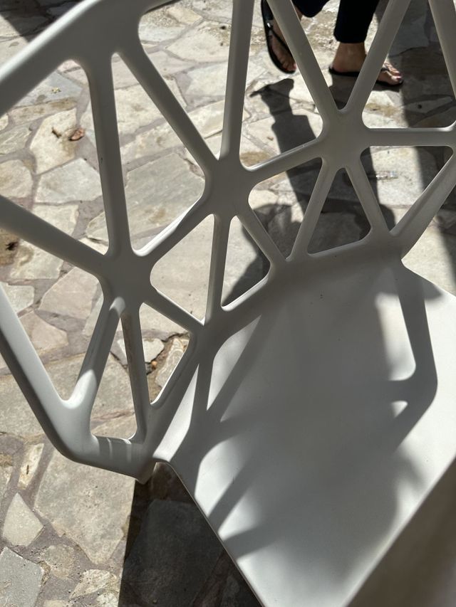 iPhone photo of white outdoor chair with shadow from patterned back on flagstone floor with lower legs of sandal wearing person walking by