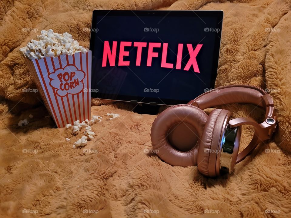 Laptop computer screen ready to watch Netflix for a fun, cozy, and relaxing night with popcorn as a snack, on soft bed blanket in room, with pink headphones