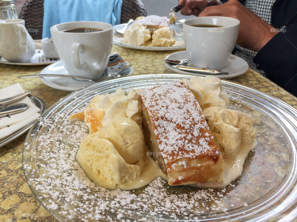 Café table with coffee cups and a glass plate with delicious Apfelstrudel with icecream and whipped cream outdoors in Germany in summer