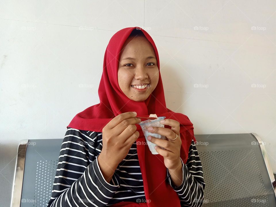 Indonesian young woman smiling, holding ice cream in her hand.