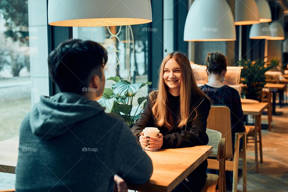 Friends having a chat, talking together, drinking coffee, sitting in a cafe. Young man and woman having a break, relaxing in cafe