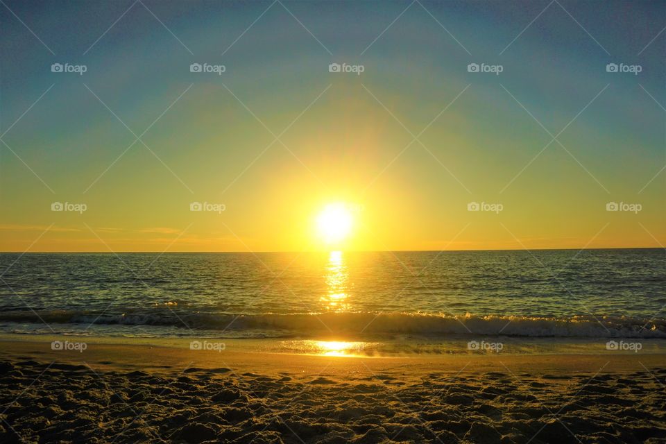 The sun rising on the horizon on a sandy beach with strong waves.