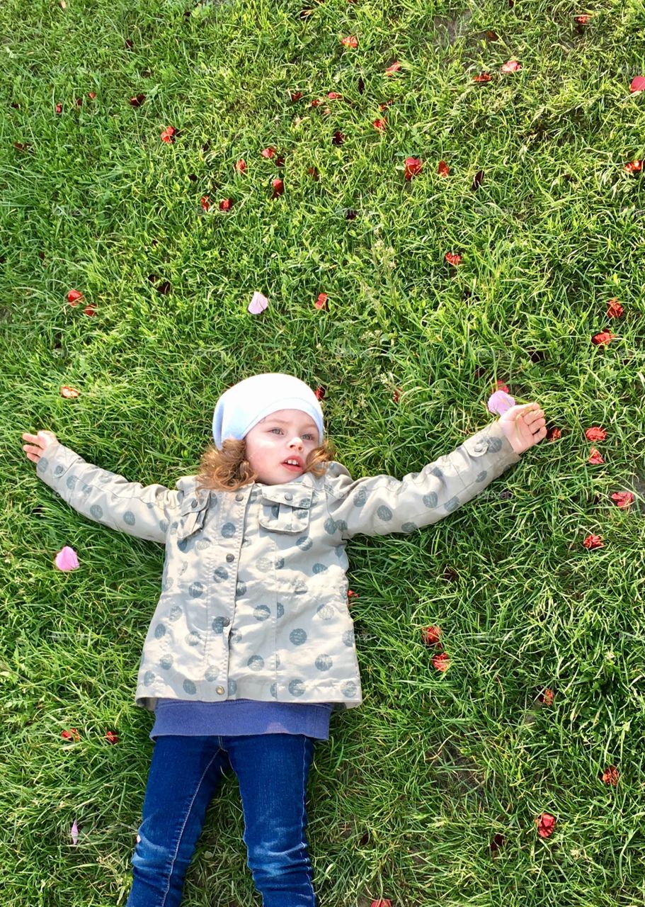 Cute curly girl laying and dreaming on the grass. Dreamy kid of my best friend. Children like her make me believe that kids are coming to us from the sky, being sent by some holy agents or angels. :) Absolutely amazing child and strong personality.