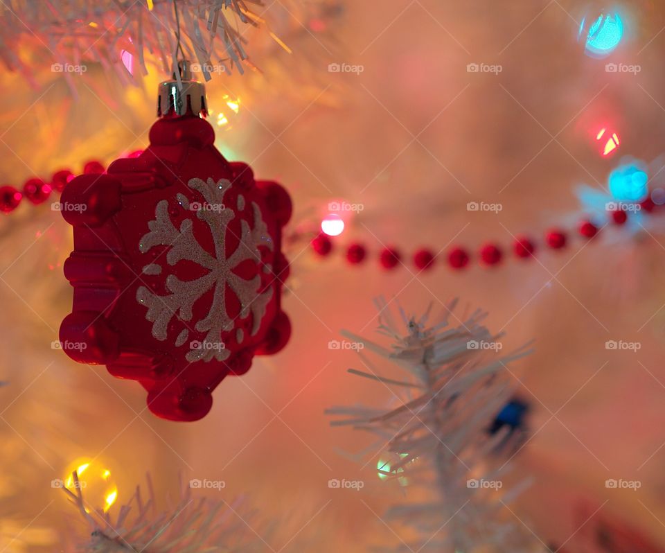 A lonely red ornament sits within a white Christmas tree that puts off a serene glow. 