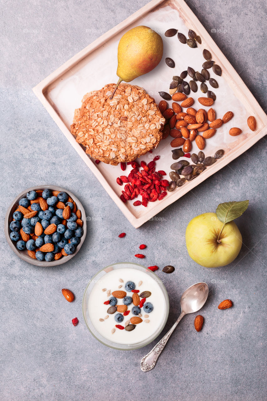 Breakfast on table. Yogurt with added blueberries and roasted almonds. Muesli cookie, apples and pears on table. Light and healthy meal. Good quality balanced diet. Flat top-down composition
