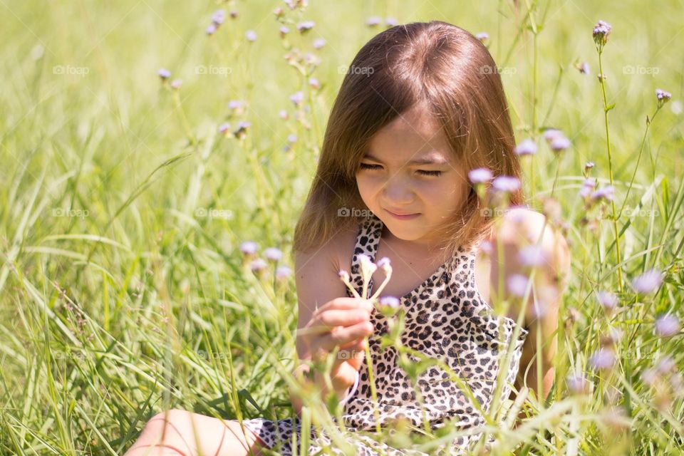 Young Girl sitting in field looking at flowers