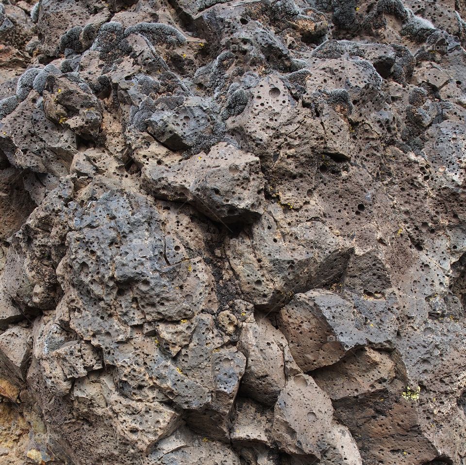 Porous jagged rocks with lots of texture, colors, and some moss  on a hillside in Central Oregon on a spring day. 
