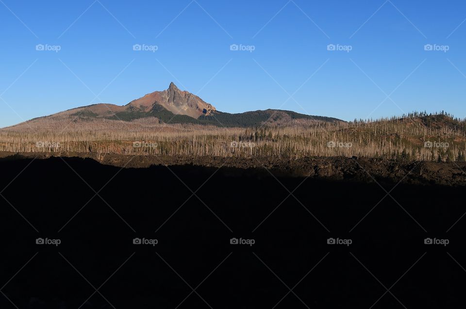 A vast lava rock field leads to the jagged peak of Mt. Washington in Oregon’s Cascade Mountain Range on a sunny fall morning with clear blue skies. 