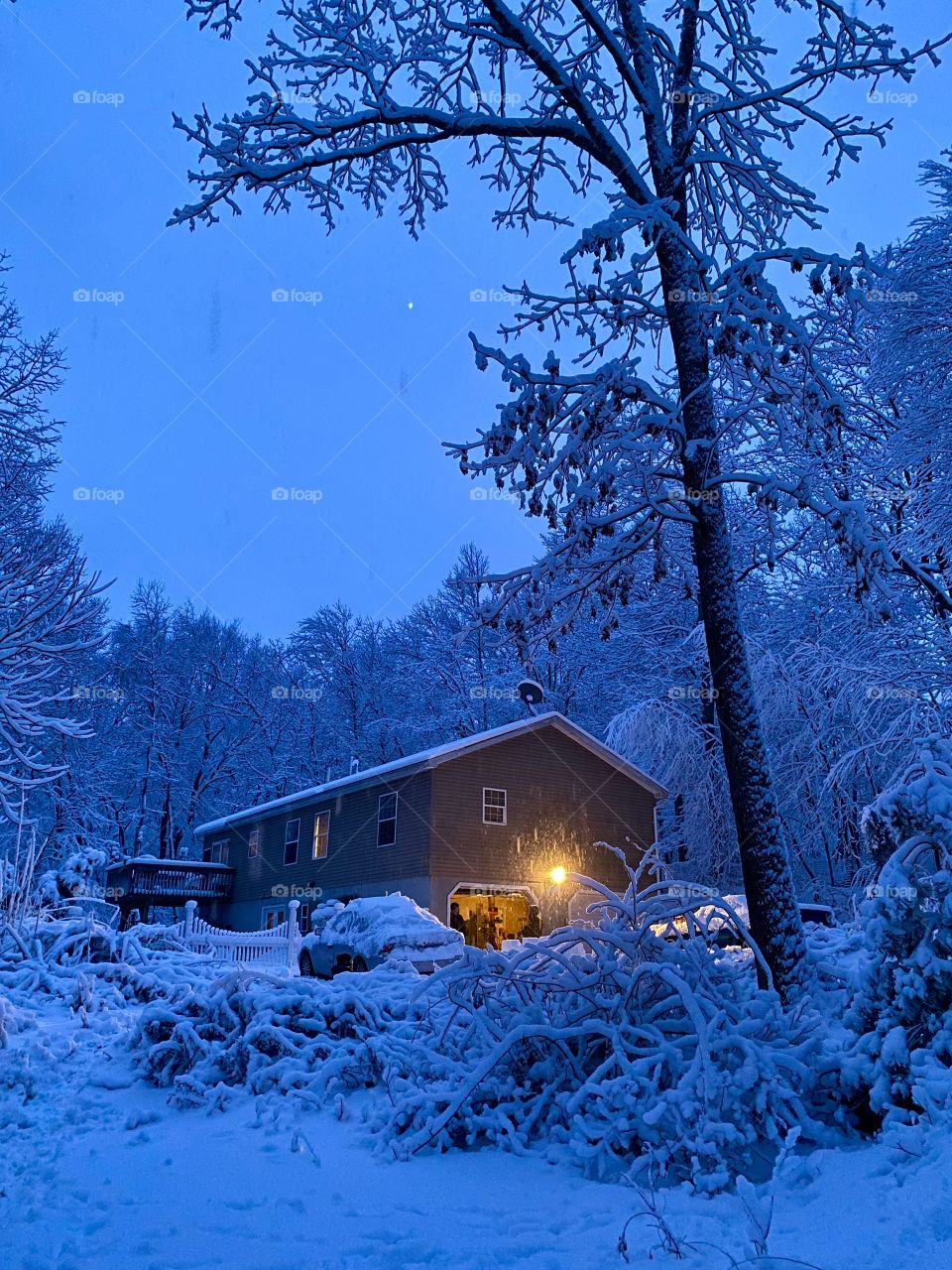 Snow covered scenery and house with garage light on during a heavy snow storm 