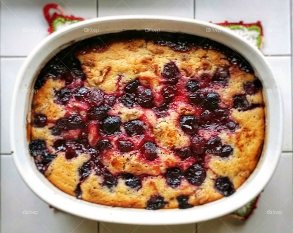 An old fashioned sweet black cherry cobbler fresh out of the oven in an oval dish on the kitchen counter