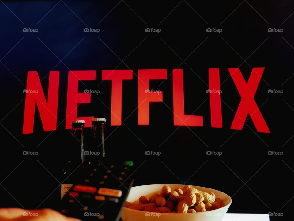 hand on the remote type Netflix on the TV ready for a night at home with beers and peanuts