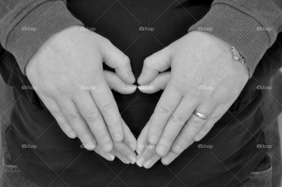 Maternity shoot. Mom and dad to be make heart shape with their hands on mommies baby bump