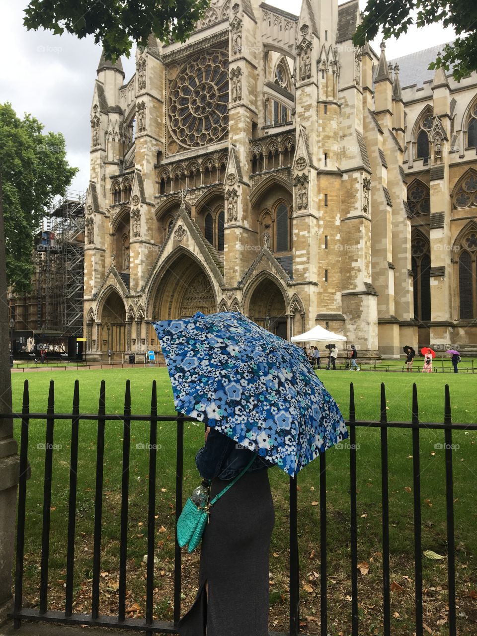 A woman stays dry under a bright blue umbrella as she walks past Westminster abbey on a rainy day