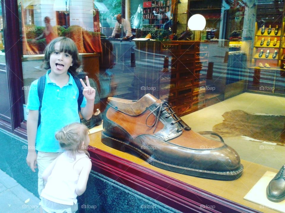 Los niños pequeños juegan y sonríen al lado de un escaparate de tienda de zapatos .