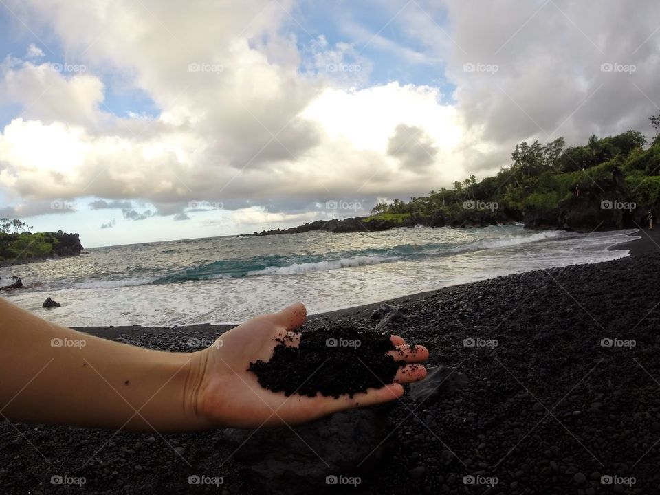 Black Sand beach Hawaii. The black sand beach in Hawaii with a hand in the foreground showing the sand in detail. 