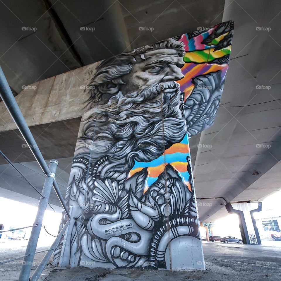 Visual street art on cement highway pillar under highway in a parking lot. Appears to be greek God of mythology Zeus.