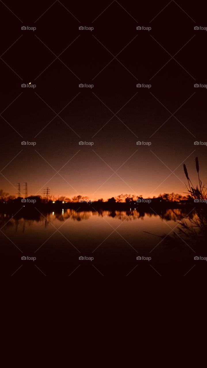 Mirrored Sunset Colors Silhouetted reflection on Lake Water Backlit to Lighthouse mixing with Night Colors. 