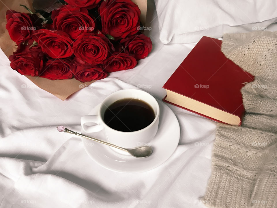 Red roses, red book, coffee cup and knitted sweater in cozy bed 