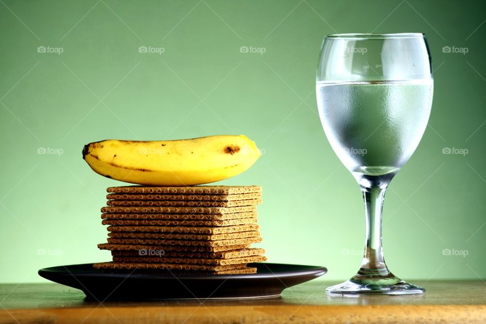 stack or pile of soda crackers, a banana and a goblet of water