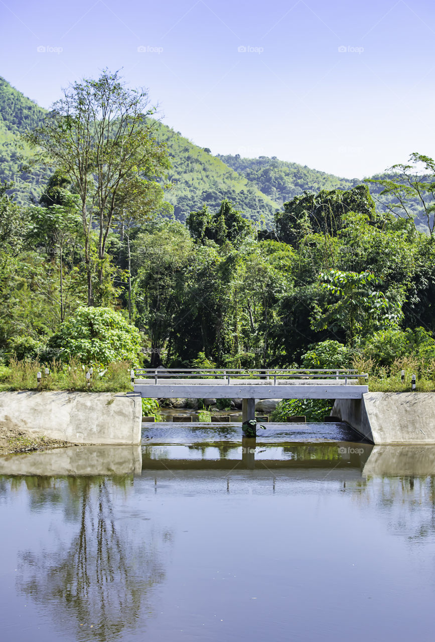 Concrete bridge over the weir in the river ,The background of mountains and trees