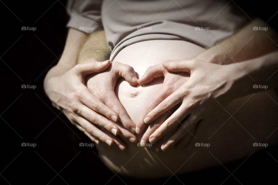 Couple making heart shape on pregnant baby