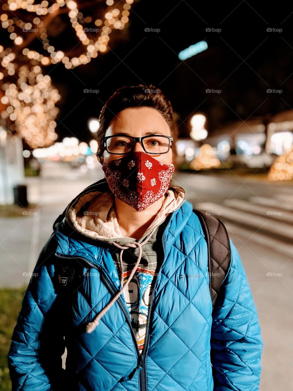 Young woman in red mask walking in city with Christmas lights alone.