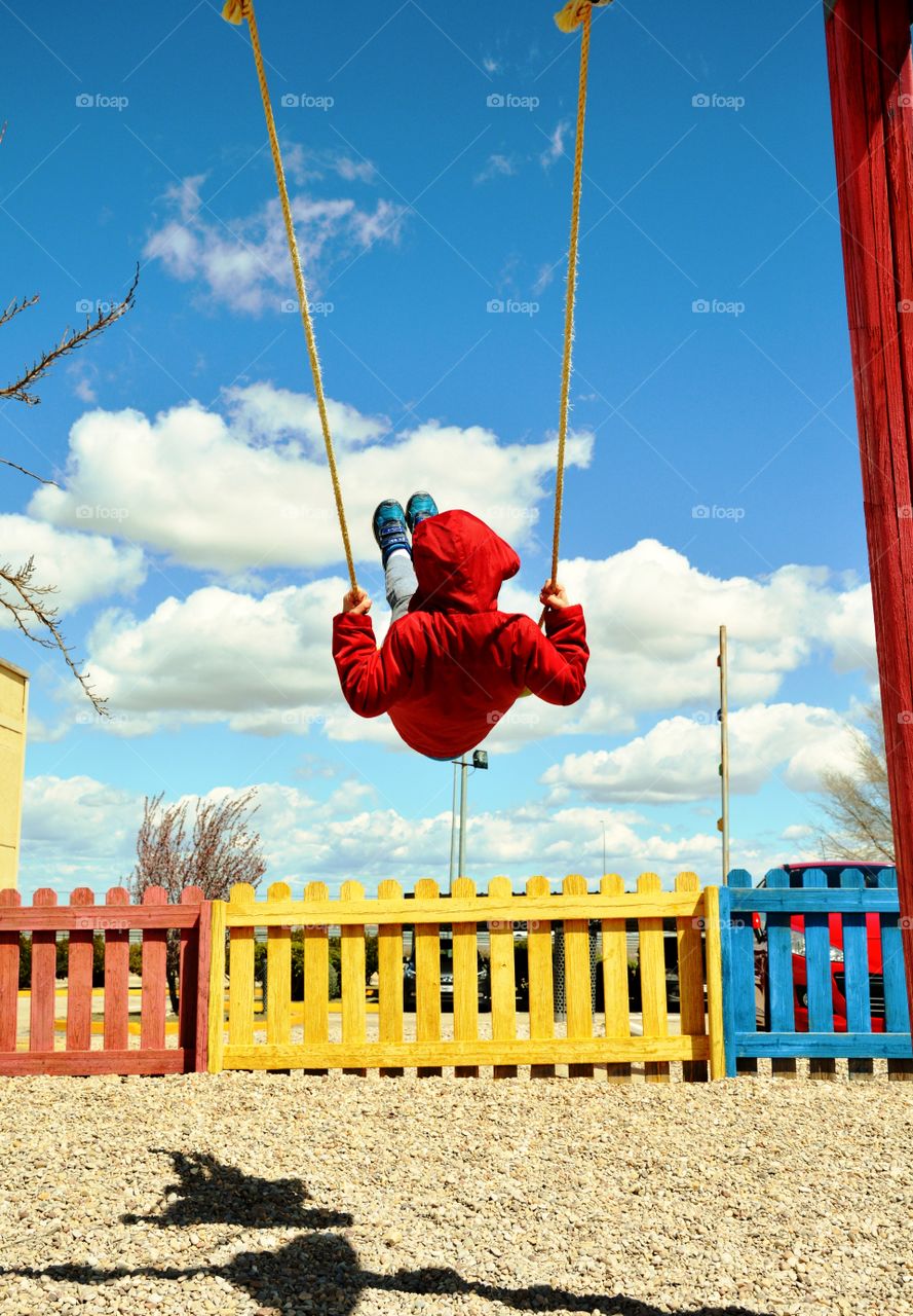 a boy swinging in a swing in a cloudy day and a coloured fence