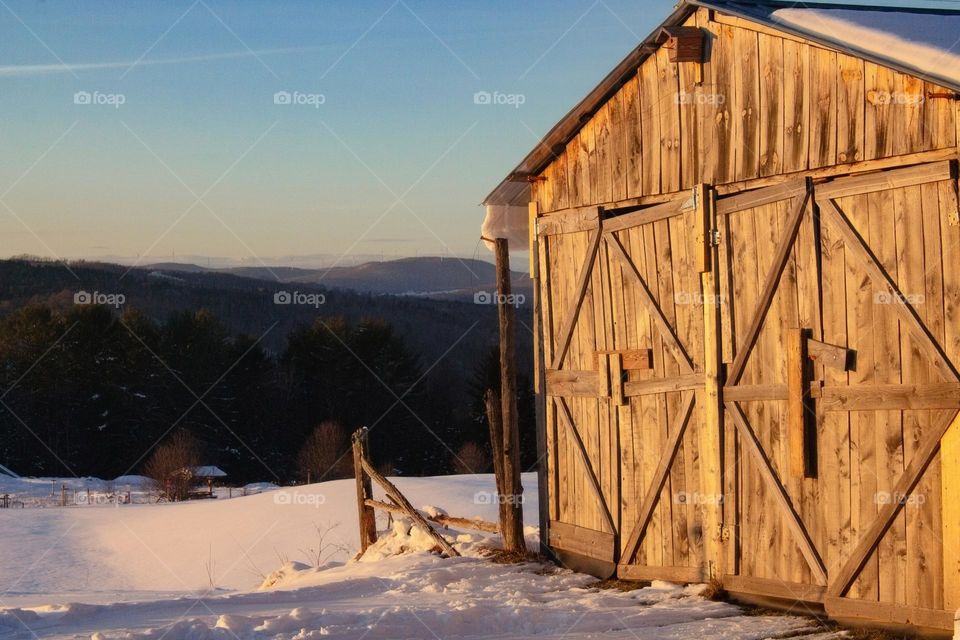 A warm wooden shed in the setting sunlight with a background of mountains and blue skies during winter in New England.
