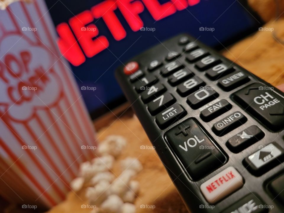 Aiming the remote control at television screen to choose favorite netflix channel to binge watch TV shows or movies for a fun and cozy night in with a popcorn snack